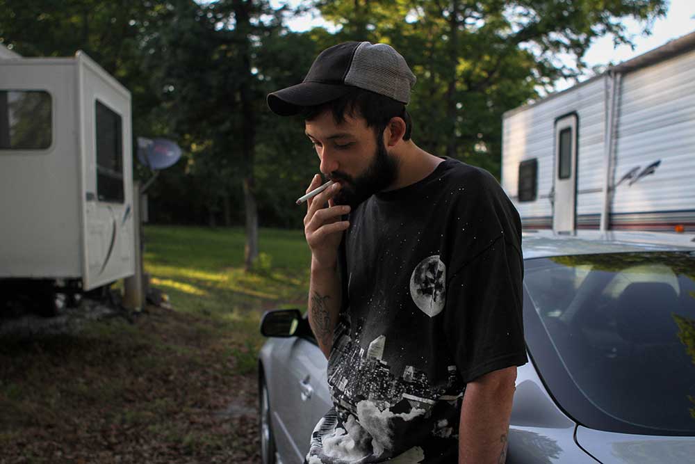 Ryan smokes a cigarette outside his father's camper.